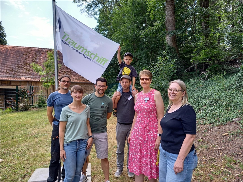 sechs Erwachsene und Kind im Grünen mit einer Fahne mit Aufschrift "Traumschiff"