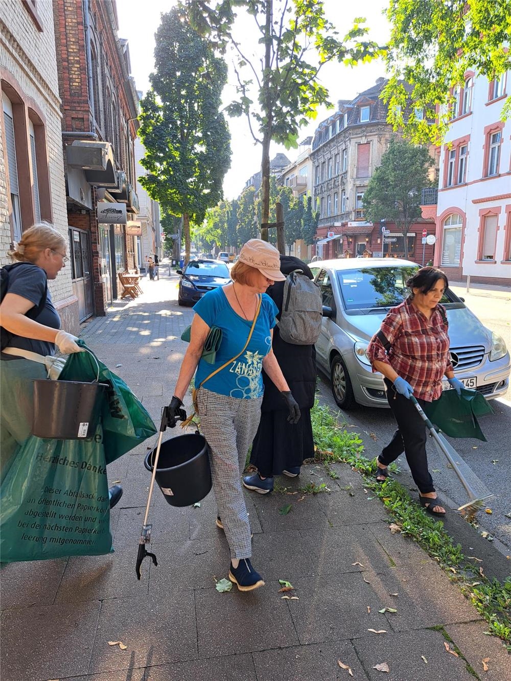 Vier Frauen gehen mit Eimern, Müllsäcken, Handschuhen und Greifzangen auf einem Bürgersteig und suchen auf dem Boden nach Müll (Daniel Naumann)