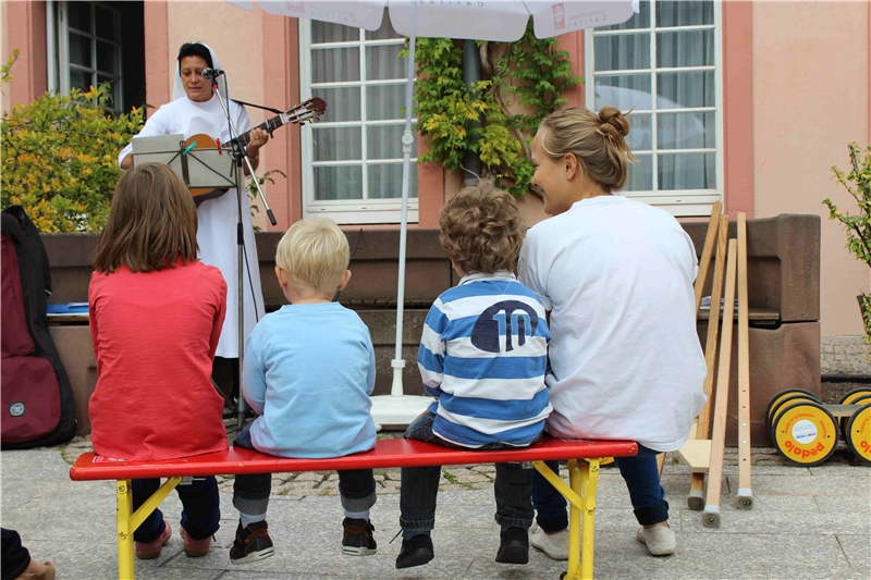  Schwester Theresia Simon vom Sankt-Rochus-Kindergarten singt zur Gitarre, mehrere Kinder sitzen auf einer Bank und hören zu oder singen mit. (Julia Gaschik)