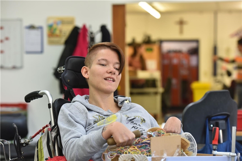 Junge Frau im Rollstuhl arbeitet in Werkstatt für Menschen mit Behinderung