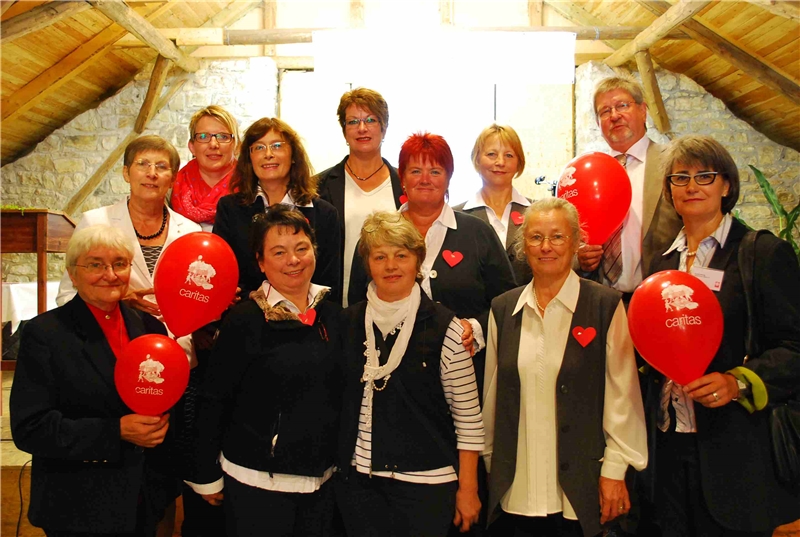 Gruppenbild Angehöriger der Caritas-Konferenz Ovenhausen im dörflichen Gemeinschaftshaus. Sie haben sich rote Herzen angesteckt und zeigen außerdem rote Luftballons mit dem Motiv des Caritas-Picknick. (Helga Krooss)