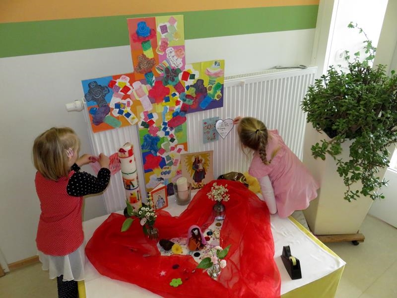 Ein Tisch mit einem selbstgebastelten Kreuz darauf und Kinder, die daneben Zettel anbringen 