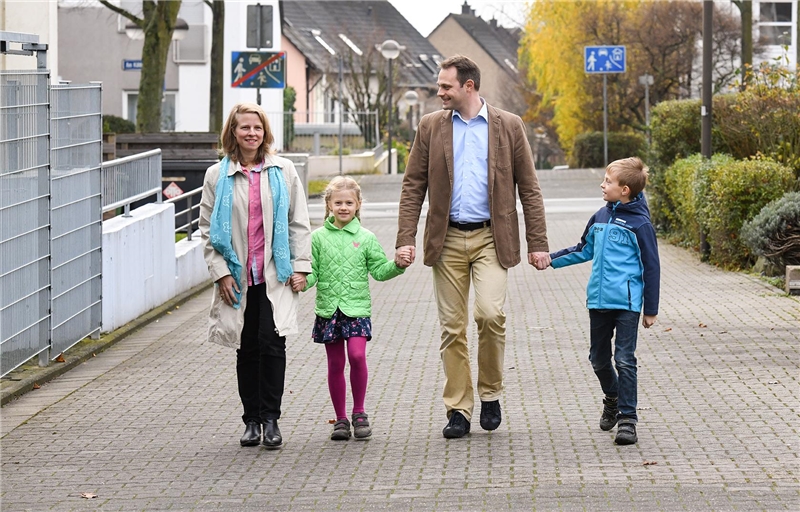 Mutter, Tochter, Vater und Sohn laufen gut gelaunt Hand in Hand die Straße entlang