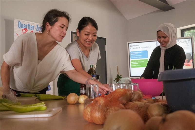 Drei Frauen stehen an einem Tisch und wählen Lebensmittel aus, die sie zum Kochen brauchen