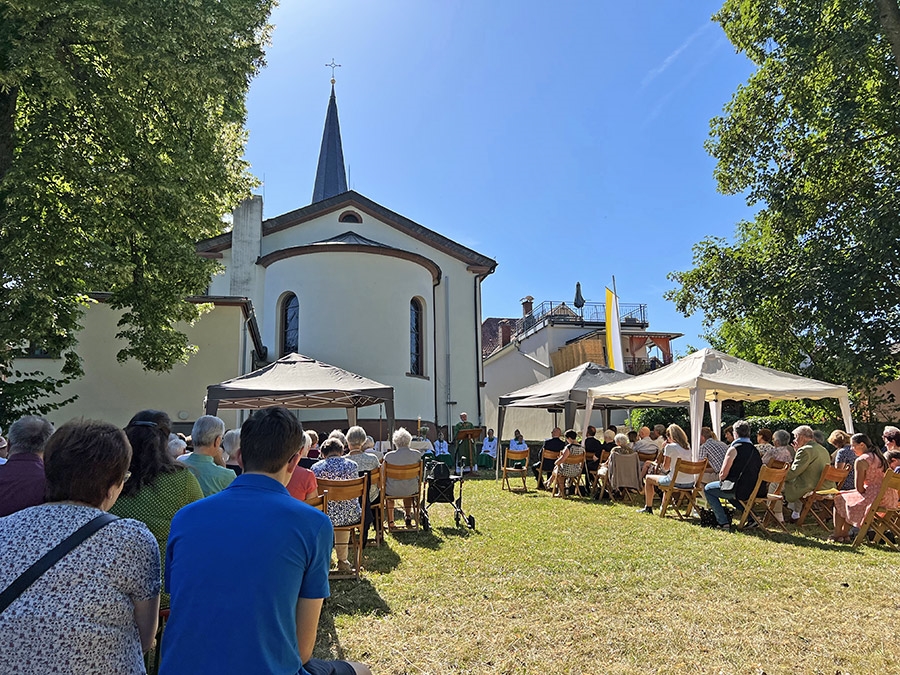 Besuchende eines Gottesdienstes im Außengelände hinter einer Kirche (Caritasverband Darmstadt e. V. / Jens Berger)