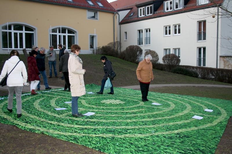 Menschen laufen über eine Matte, auf der in Labyrinth abgebildet ist 