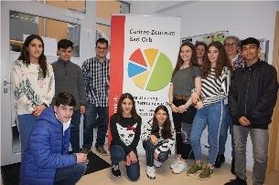 Eine Gruppe Jugendlicher sowie drei Erwachsene stehen neben einem Plakat des Caritas-Zentrums (Jutta Link)