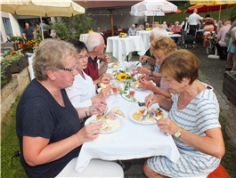 Einige Menschen sitzen im Garten an einem Tisch und essen / Foto: Schedlbauer