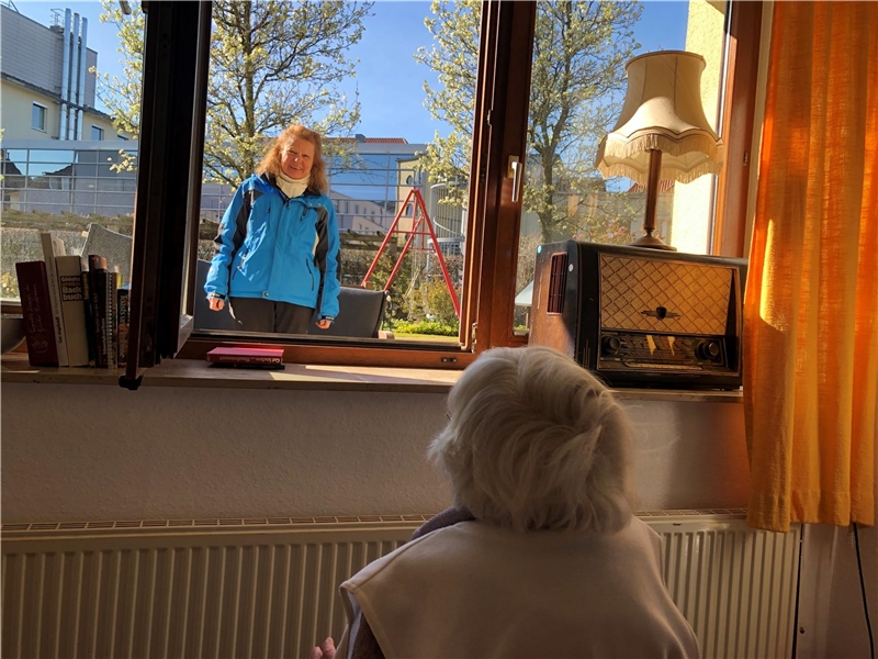 Das Foto zeigt eine Frau vor einem Fenster, im Raum sitzt eine alte Dame davor.