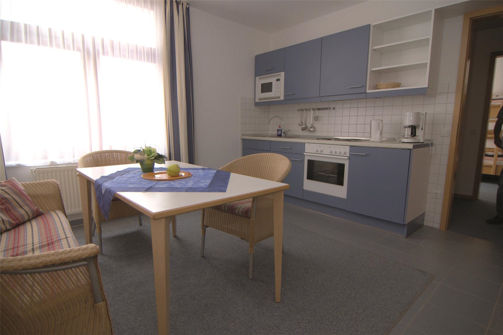 Eine blaue Küchenzeile und eine Essecke mit Korbmöbeln in einem Gästezimmer. 
