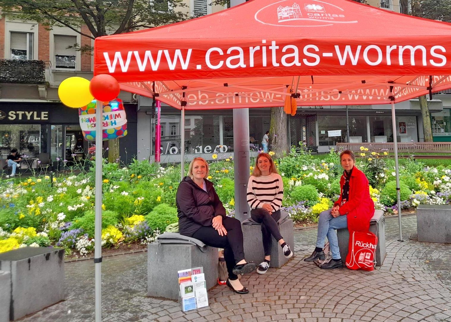 drei Frauen unter einem roten Caritas-Pavillon auf einer Bank