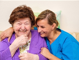Eine Pflegerin umarmt eine Seniorin, die neben ihr sitzt. / Werner Krüper