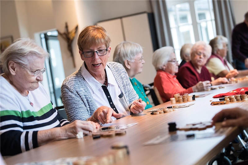 An einem langen Tisch sitzen ältere Damen gemeinsam und spielen ein Brettspiel