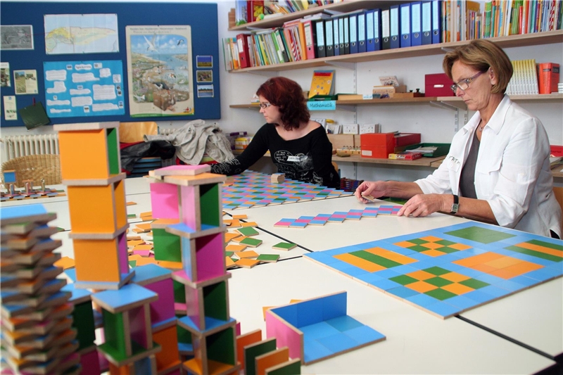 Das Foto zeigt zwei Frauen an einem Tisch, die bunte Figuren zu symmetrischen Mustern zusammen legen.