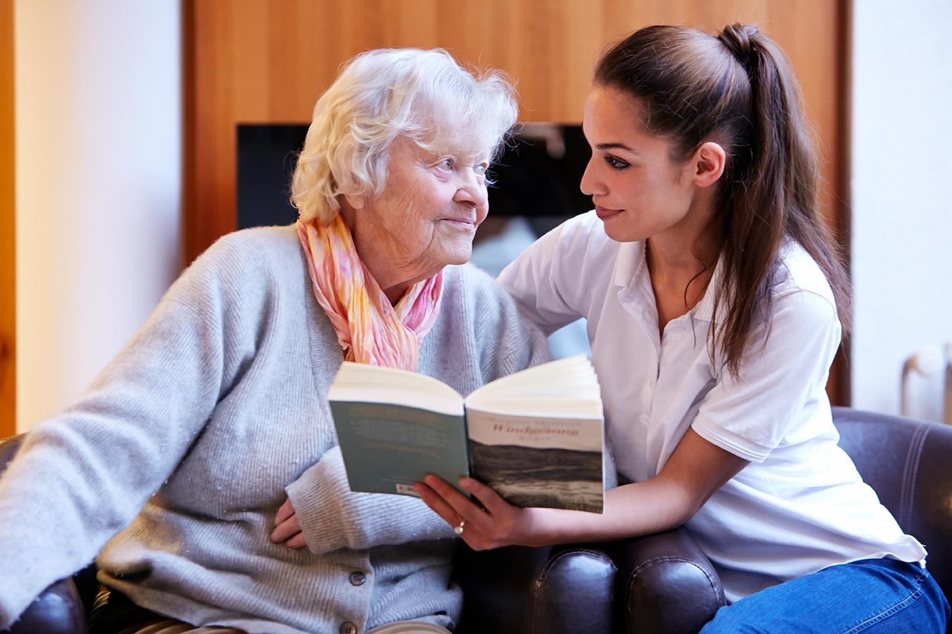 Junge Frau schaut sich mit alter Frau ein Buch an