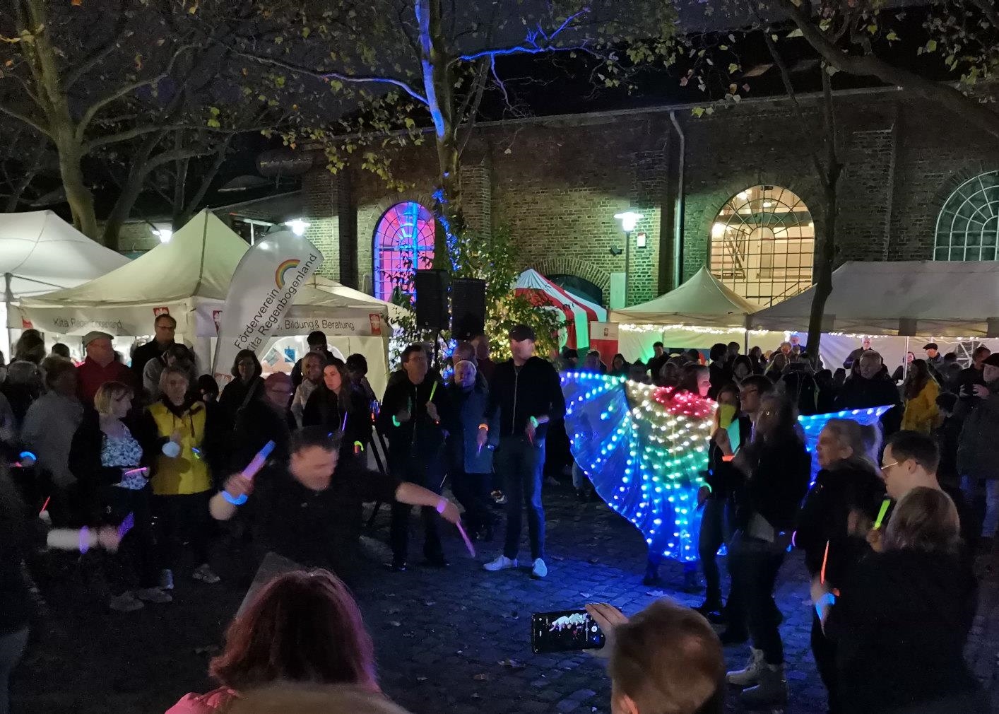 Tänzer mit Leuchtarmbändern und leuchtendem Umhang bei den Novemberlichtern 2022. 
