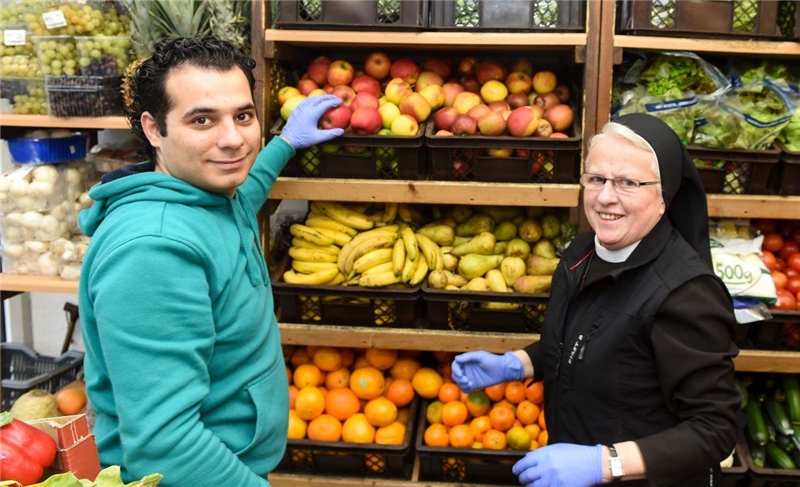 Ordensfrau und Mann mit Migrationshintergrund sortieren Obst in einem Caritas-Laden