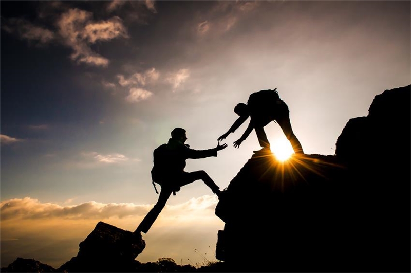 Ein Mann hilft einem anderen auf einen Berg zu steigen. 