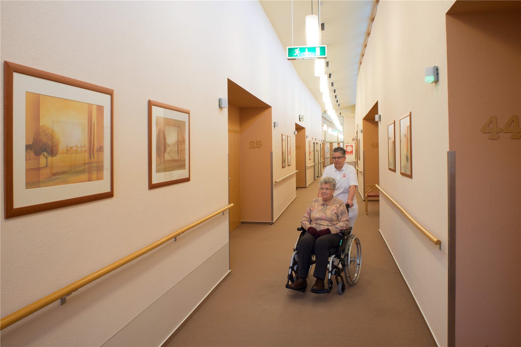 Pflegekraft und Seniorin m Rollstuhl in einem hellen Flur. (Udo Keus)