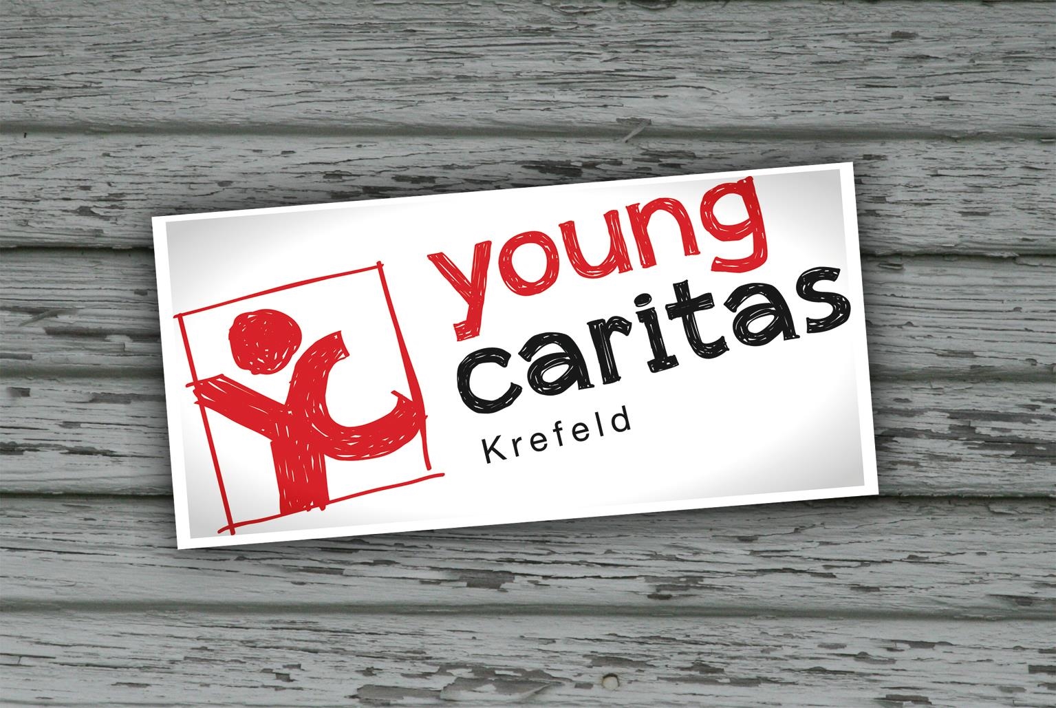 Das Logo der youngcaritas Krefeld in einem weißen Kasten auf einem Holz-Hintergrund