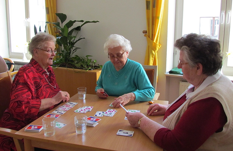 Drei Bewohnerinnen sitzen am Tisch und spielen zusammen Karten. 