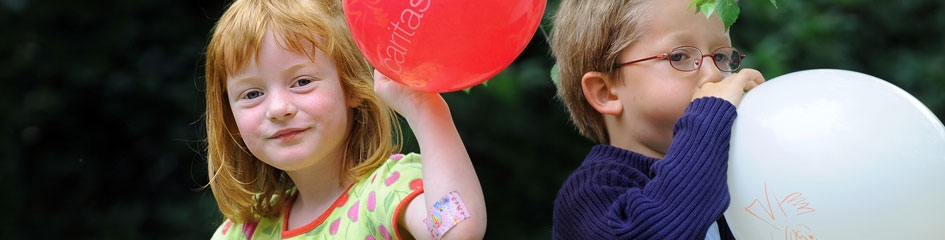 Junge und Mädchen mit Caritas-Luftballons