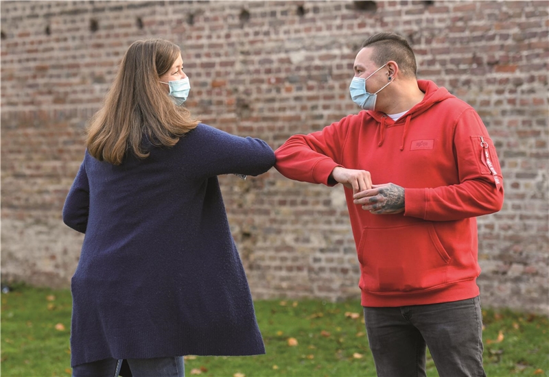 Zwei Menschen mit Mundschutz begrüßen sich mit einem Ellenbogenstubser