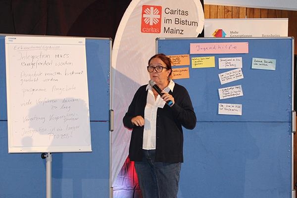 Frau Lehnard mit Mikrofon auf der Bühne vor Pinnwänden mit gesammelten Ideen (Caritasverband Darmstadt e. V.)