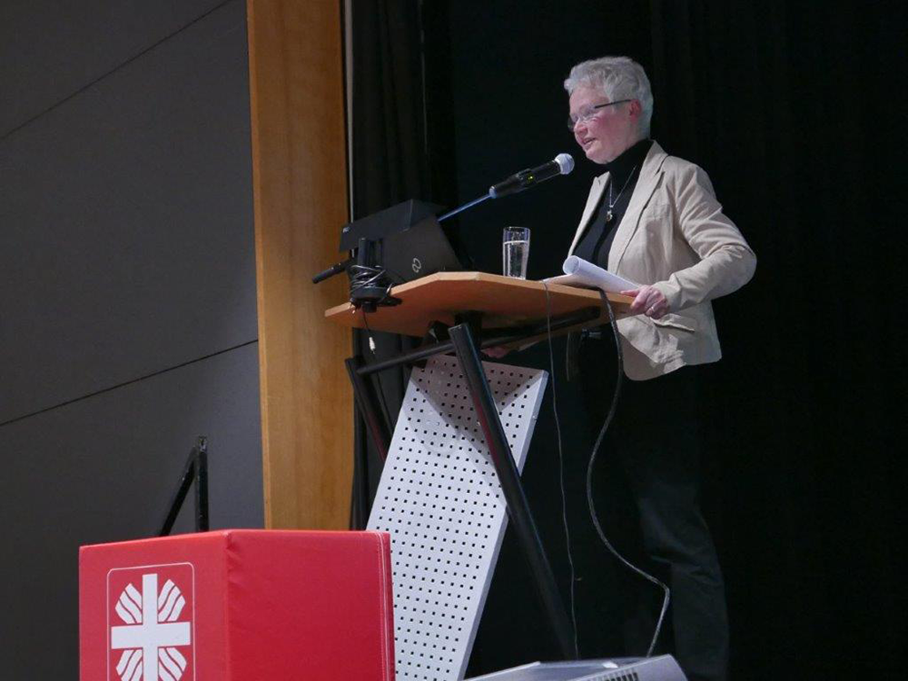 Prof. Gertrud Hundenborn steht vor einem Pult und hält ihre Präsentation auf der Informationsveranstaltung 'Das neue Pflegeberufegesetz' in Dortmund. Vor dem Pult steht ein roter Caritas-Würfel. (Jürgen Sauer)