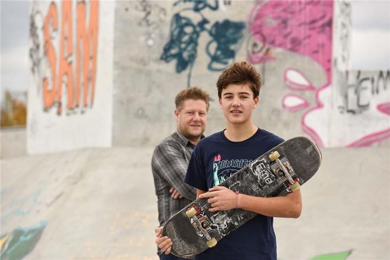 Ein Quartiersarbeiter und ein Junge mit einem Skateboard stehen in einem Skatepark