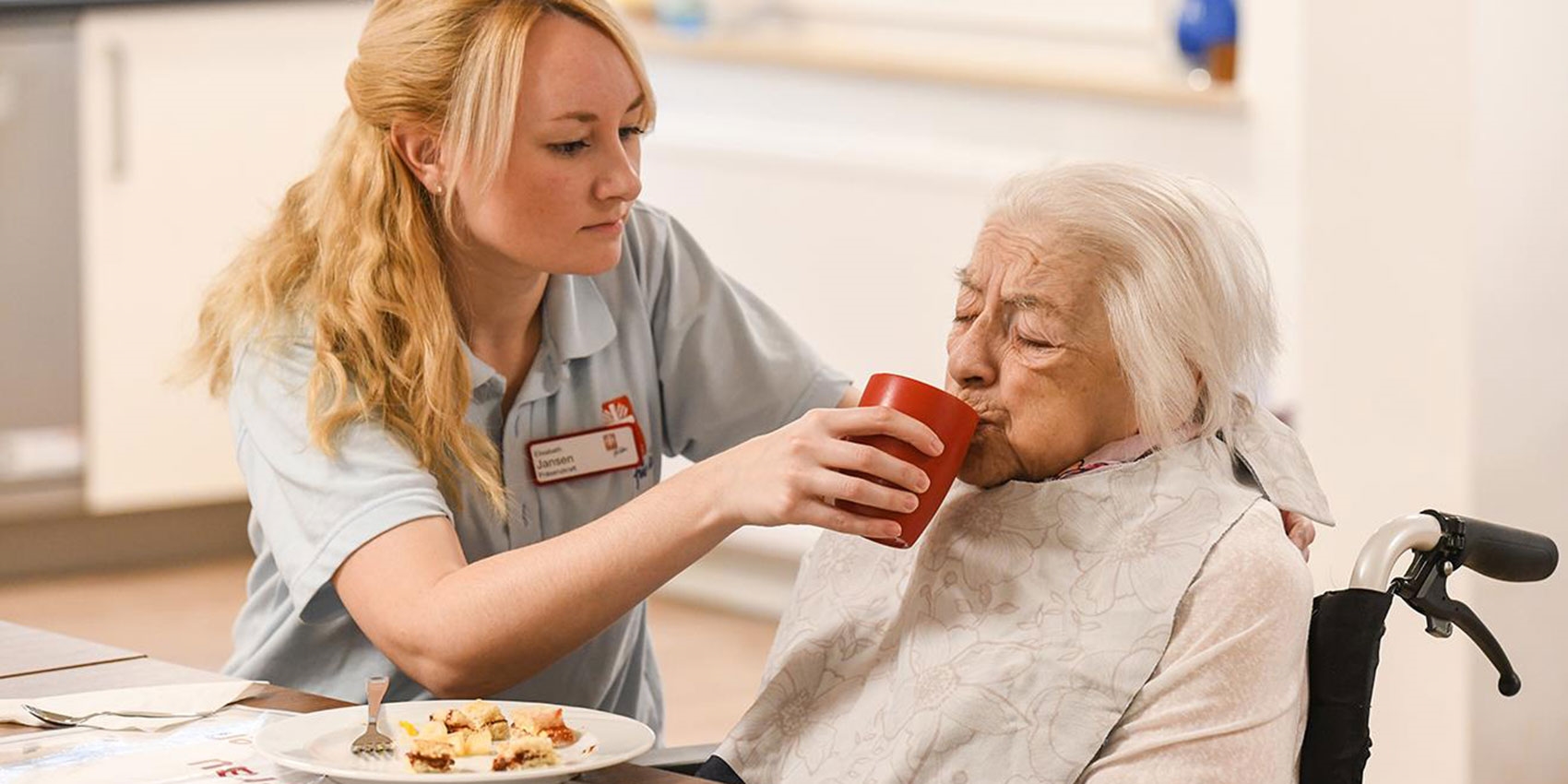 Pflegerin hilft Bewohnerin eines Pflegeheims beim Essen