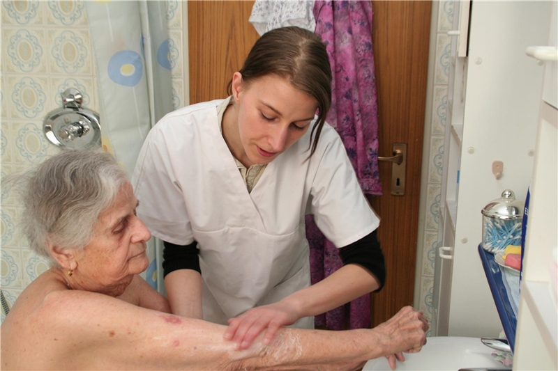 Das Foto zeigt eine Pflegerin, die einer alten Frau den Arm wäscht.