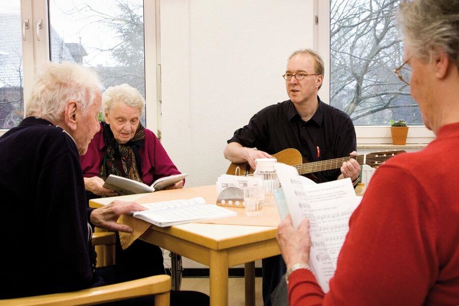 Einige Bewohner sitzen um einen Tisch und singen, jemand spielt Gitarre 