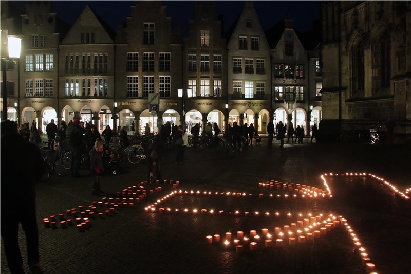 Das Foto zeigt einen Teil des Caritas-Logos als leuchtendes Kerzenbild im Dunkeln.