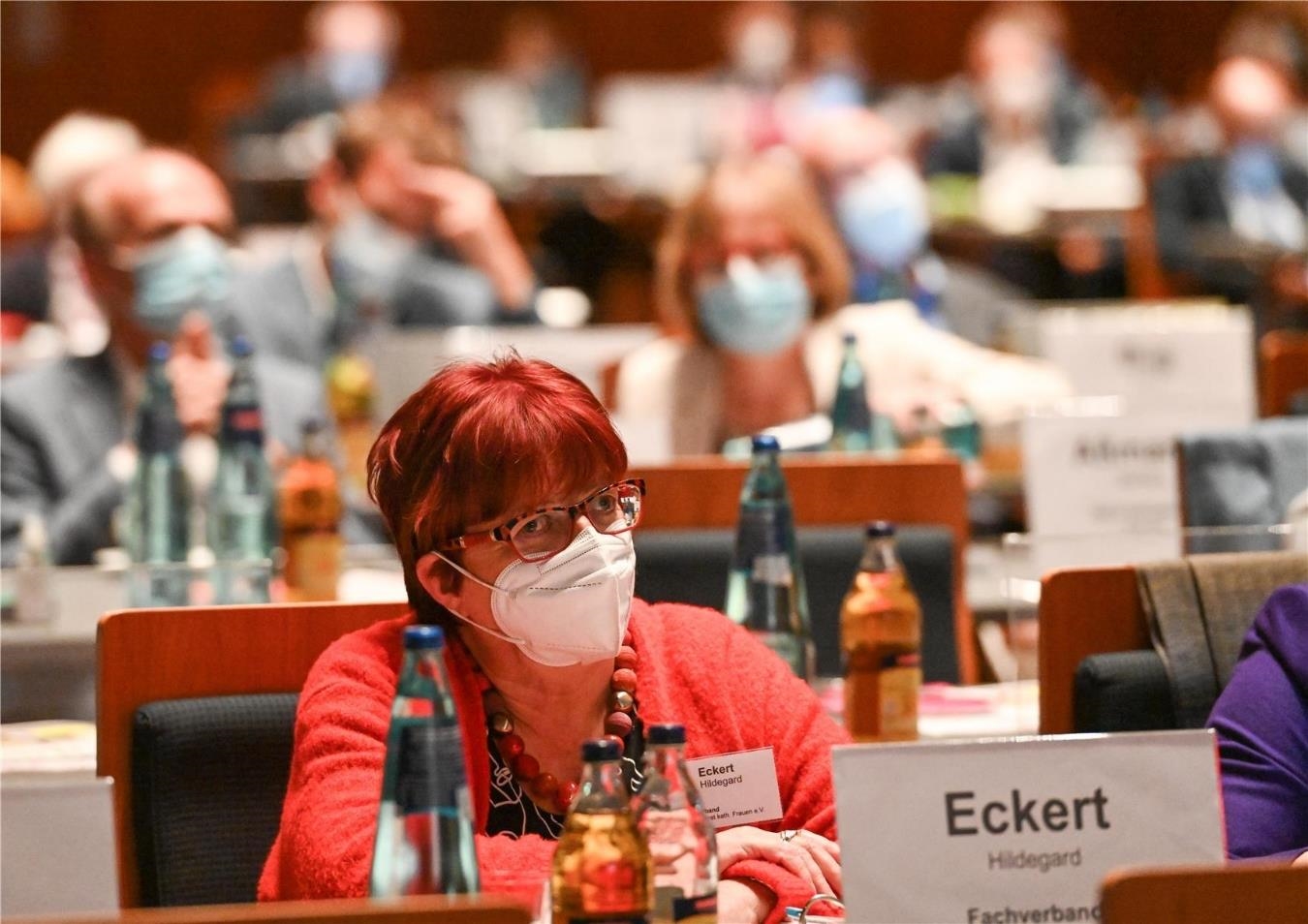Frau mit kurzen roten Haaren und Brille sitzt an einem langen Tisch. Vor ihr ein Namensschild.  (Deutscher Caritasverband / Harald Oppitz)