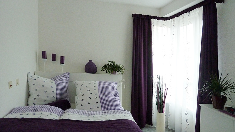 Helles Schlafzimmer mit auberginefarbener Dekoware in einer Wohnung im Servicewohnen. 
