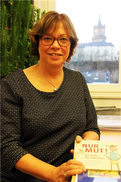 Das Porträtfoto zeigt eine vor einem Fenster sitzende Frau, die ein Buch in der Hand hält.