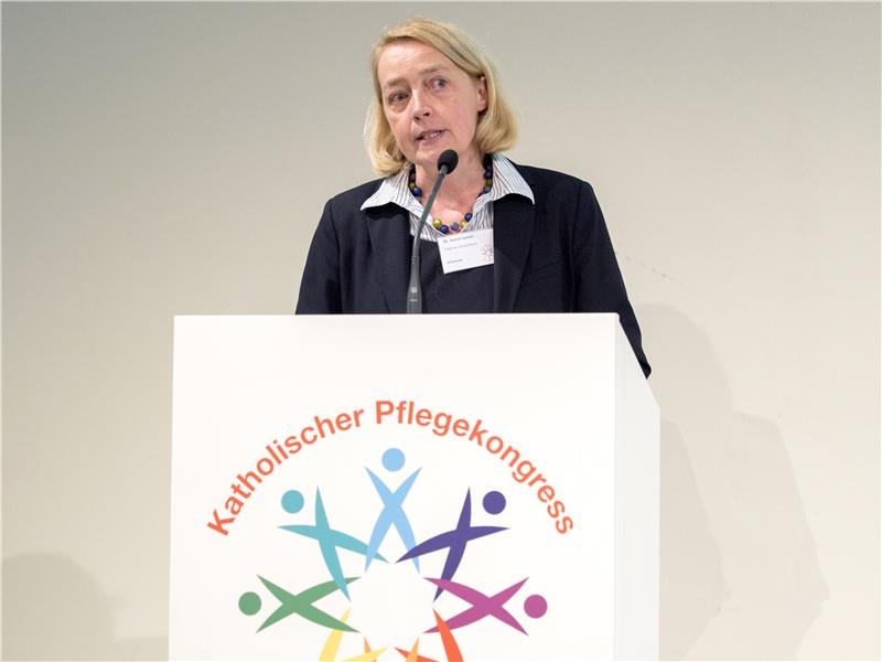 Eine blonde Frau mit halblangen Haaren steht am Rednerpult mit dem Emblem des Katholischen Pflegekongresses (Angela Kröll)