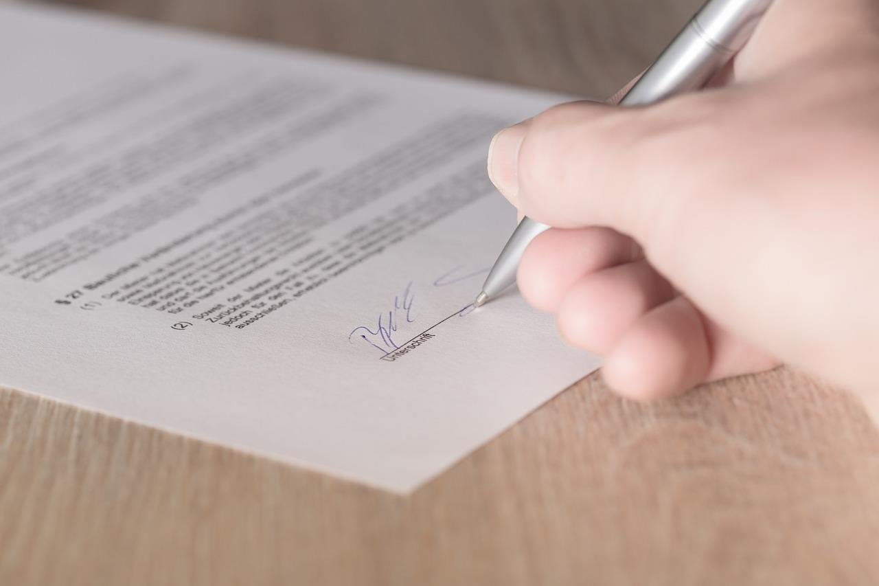 Hand, die mit einem Stift auf einem Blatt Papier unterschreibt