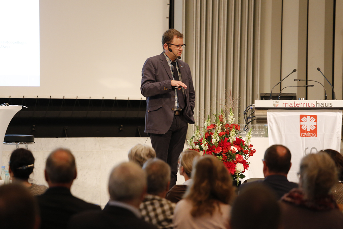 Prof. Dr. Ralf Haderlein steht beim Fachforum 'Von der Kunst, ein christliches Unternehmen zu führen' auf einer Bühne und hält einen Vortrag (Martin Karski)