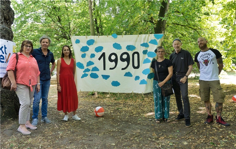 Mehrere Menschen stehen vor einem Banner mit der Zahl "1990"