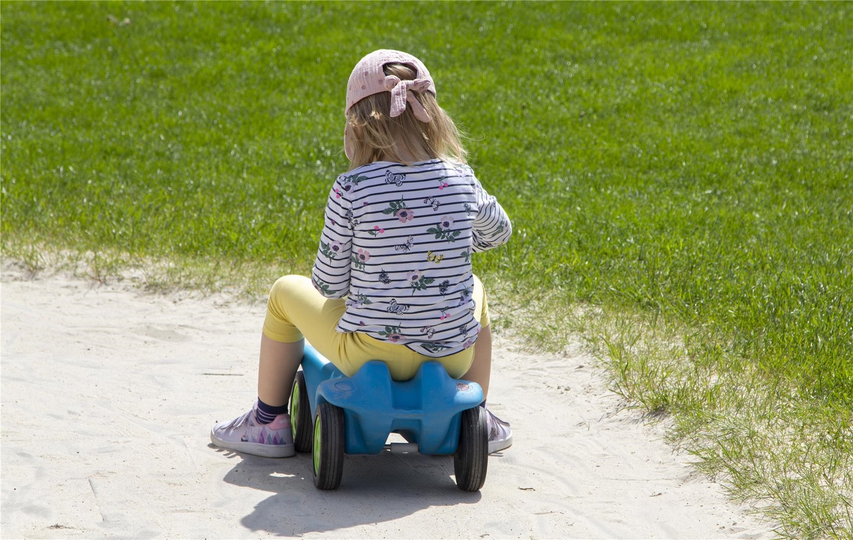 Ein kleines Mädchen sitzt auf einem Bobbycar. 