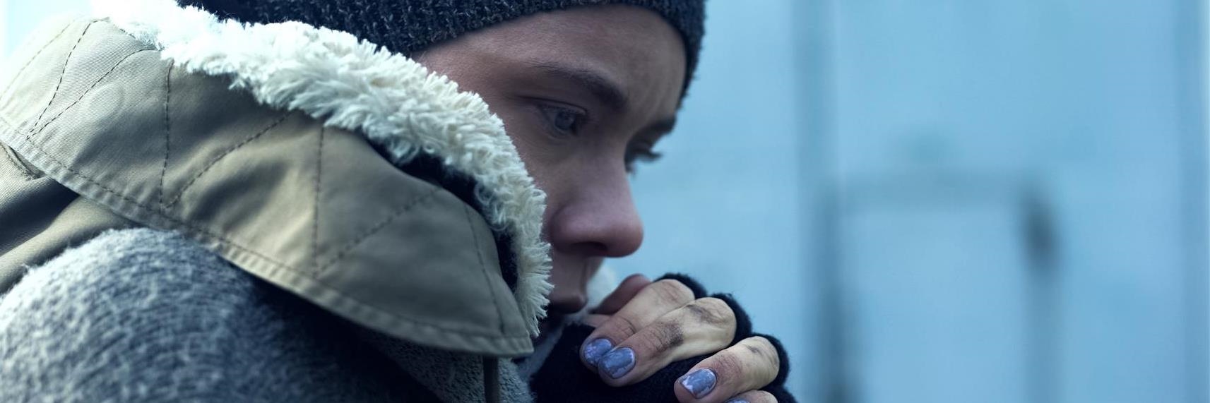 Eine junge Frau in Winterkleidung und mit dreckigen Händen schaut nachdenklich