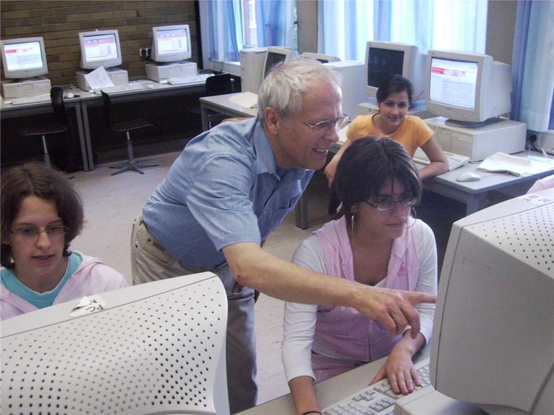 Älterer Herr gibt Jugendlichen an Computerbilschirmen Tipps zur Bewerbung