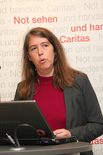 Katrin Gerdsmeier steht vor einem aufgeklappten Laptop an einem Pult und hält eine Rede. Im Hintergrund ist ein Caritas-Rollup zu sehen. (Harald Westbeld)