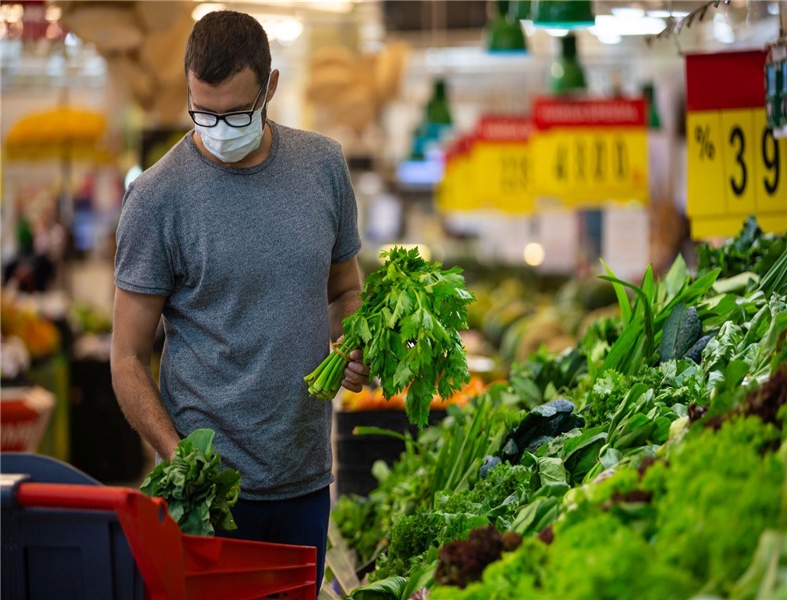 Mann mit Schutzmaske kauft Gemüse ein
