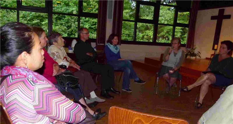 Eine Gruppe von Gästen sitzt im Halbkreis um eine Frau, die von ihrer Migrationsbiografie erzählt. (Klemens Bögner)