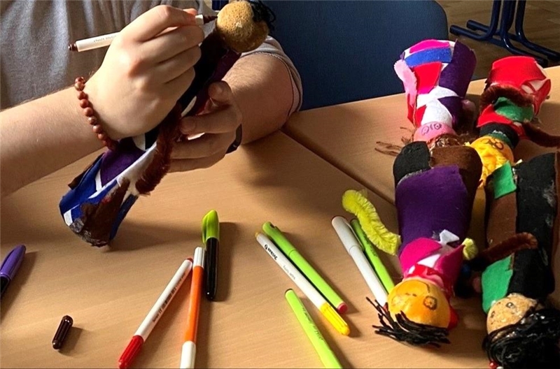 Ausschnitt von Stiften und gebastelten Puppen, denen Gesichter aufgemalt werden