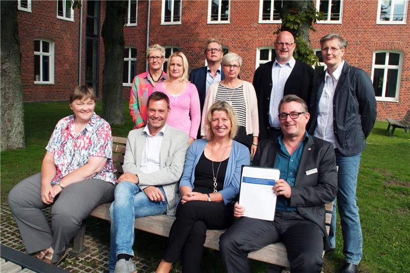 Ein Gruppenbild. Vier Personen sitzen im Vordergrund auf der Bank, sechs Personen stehen dahinter.