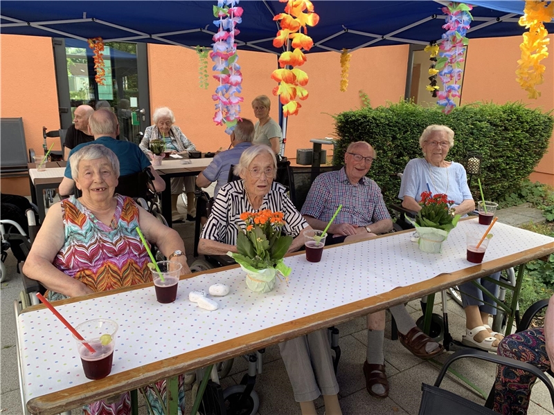 Senior:innen sitzen gemeinsam an bunt geschmückten Bierzelttischen .